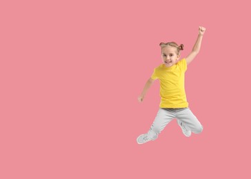 Cute girl jumping on pink background, space for text