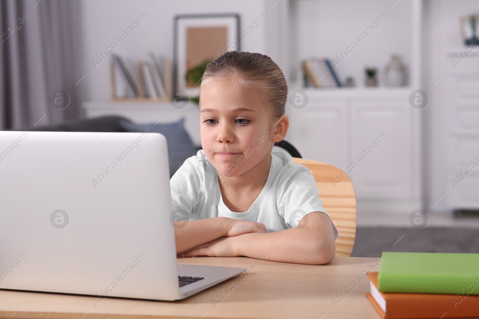 Photo of Little girl using laptop at table indoors. Internet addiction