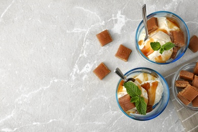 Photo of Glasses of delicious ice cream with caramel sauce, candies and mint on light grey marble table, flat lay. Space for text