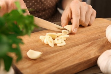 Photo of Woman cutting fresh garlic at table, closeup