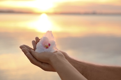 Couple with beautiful flower near river at sunset, closeup. Nature healing power