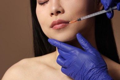 Photo of Woman getting lip injection on brown background, closeup