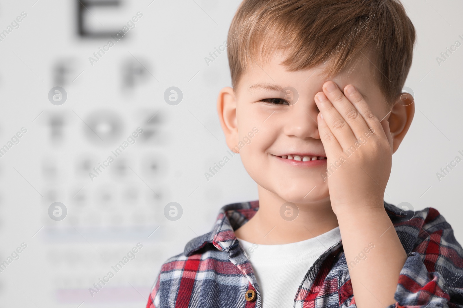 Photo of Little boy covering her eye against vision test chart