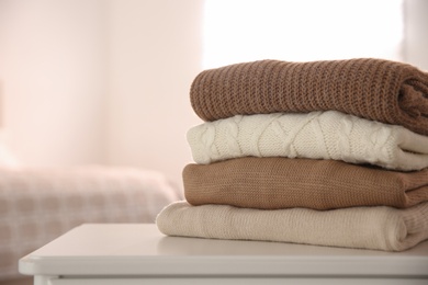 Photo of Stack of folded warm sweaters on white table indoors. Space for text