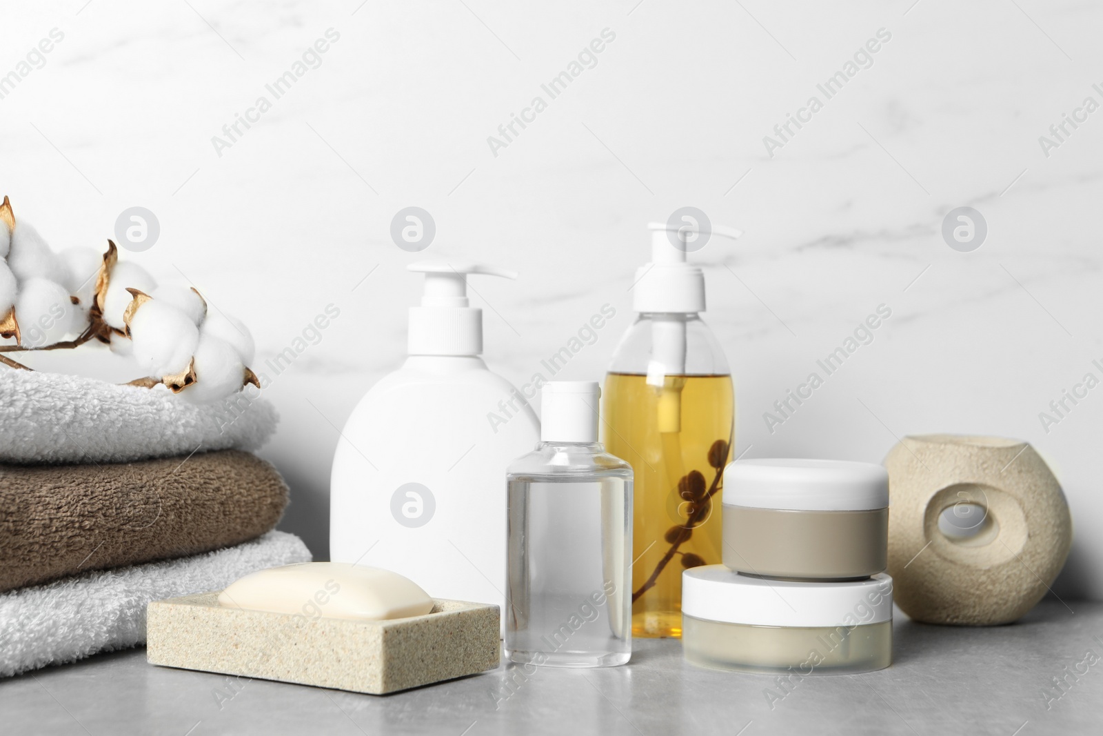 Photo of Bath accessories. Personal care products, terry towels and cotton flowers on gray table near white marble wall