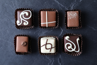 Different tasty chocolate candies on black table, flat lay