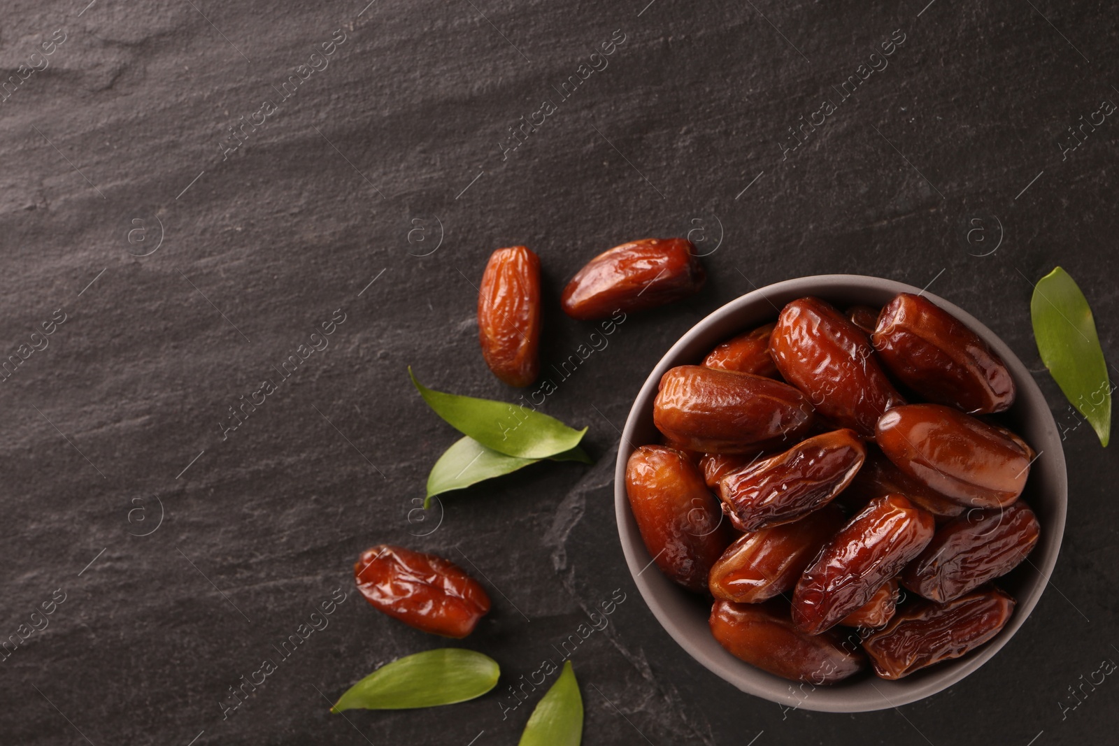 Photo of Tasty sweet dried dates and green leaves on black table, flat lay. Space for text