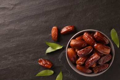 Photo of Tasty sweet dried dates and green leaves on black table, flat lay. Space for text