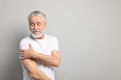 Arthritis symptoms. Man suffering from pain in shoulder on gray background, space for text