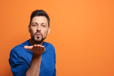 Photo of Handsome man blowing kiss on orange background. Space for text