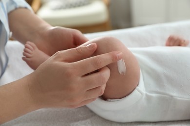 Photo of Mother applying body cream on her little baby indoors, closeup
