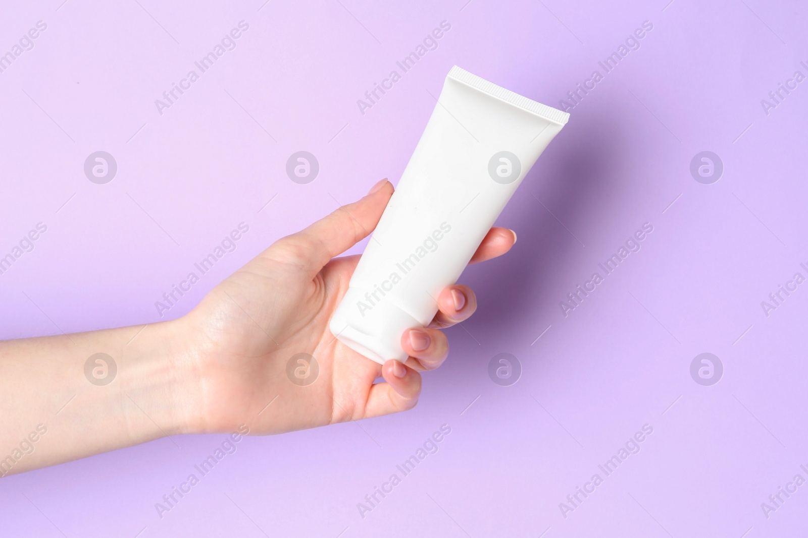 Photo of Woman holding tube of cream on violet background, closeup