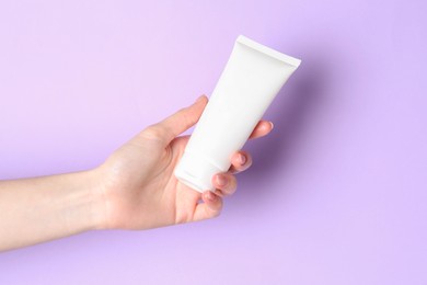 Woman holding tube of cream on violet background, closeup