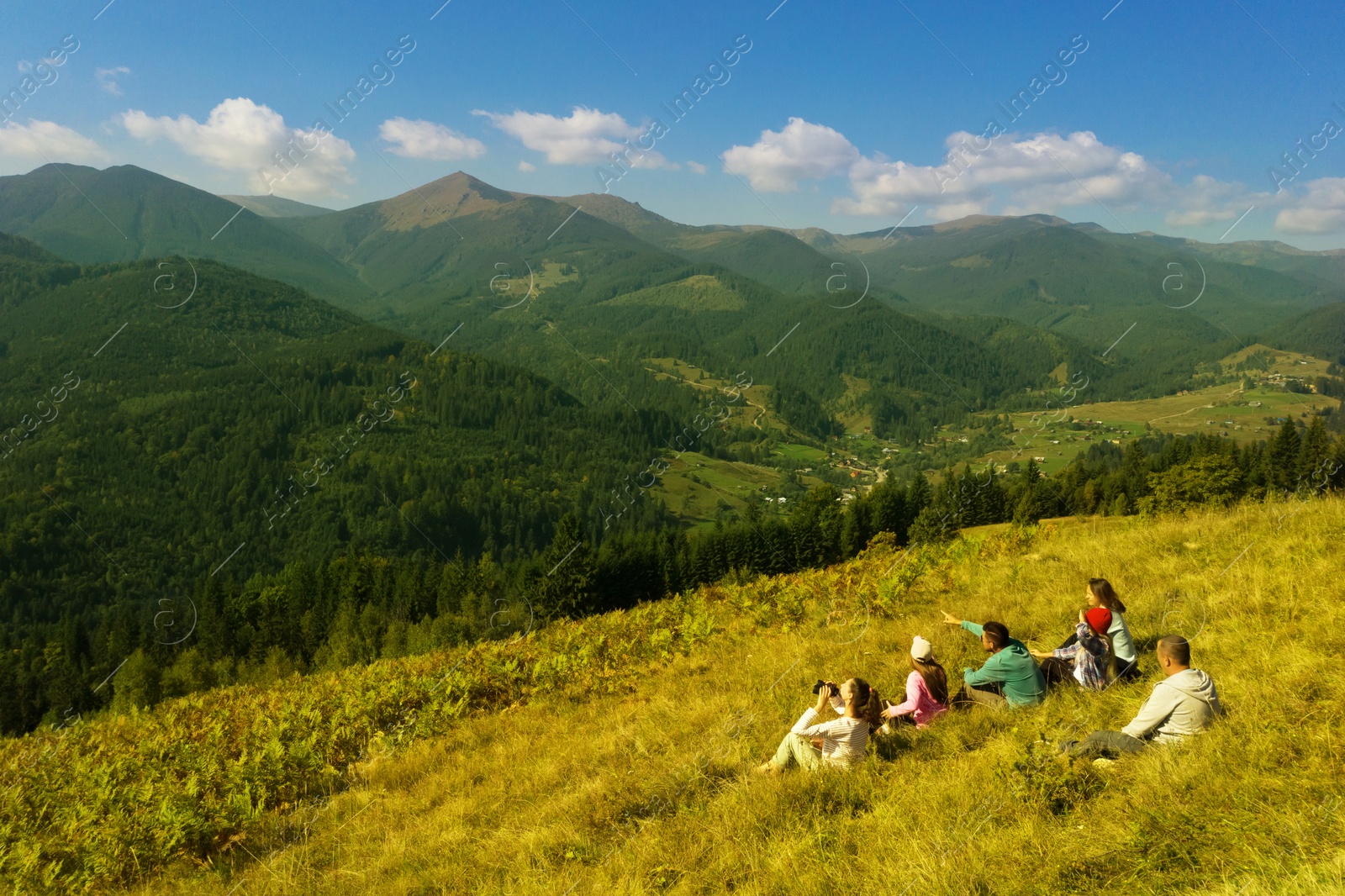 Image of Group of tourists sitting on hill in mountains