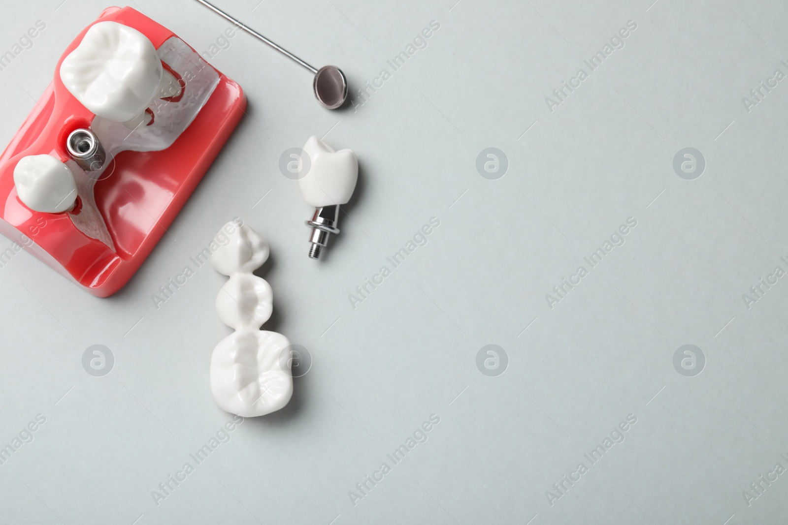 Photo of Educational model of gum with post between teeth, dental implant and mirror on grey background, flat lay. Space for text