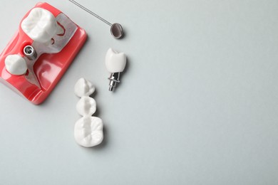 Photo of Educational model of gum with post between teeth, dental implant and mirror on grey background, flat lay. Space for text