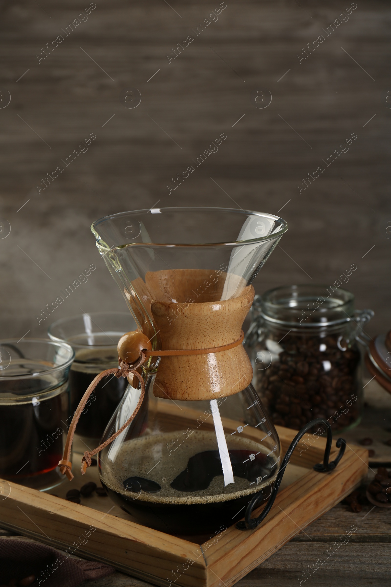 Photo of Glass chemex coffeemaker with coffee and beans on wooden table