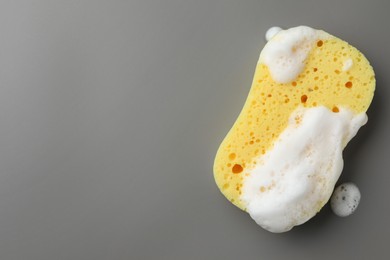 Yellow sponge with foam on grey background, top view. Space for text