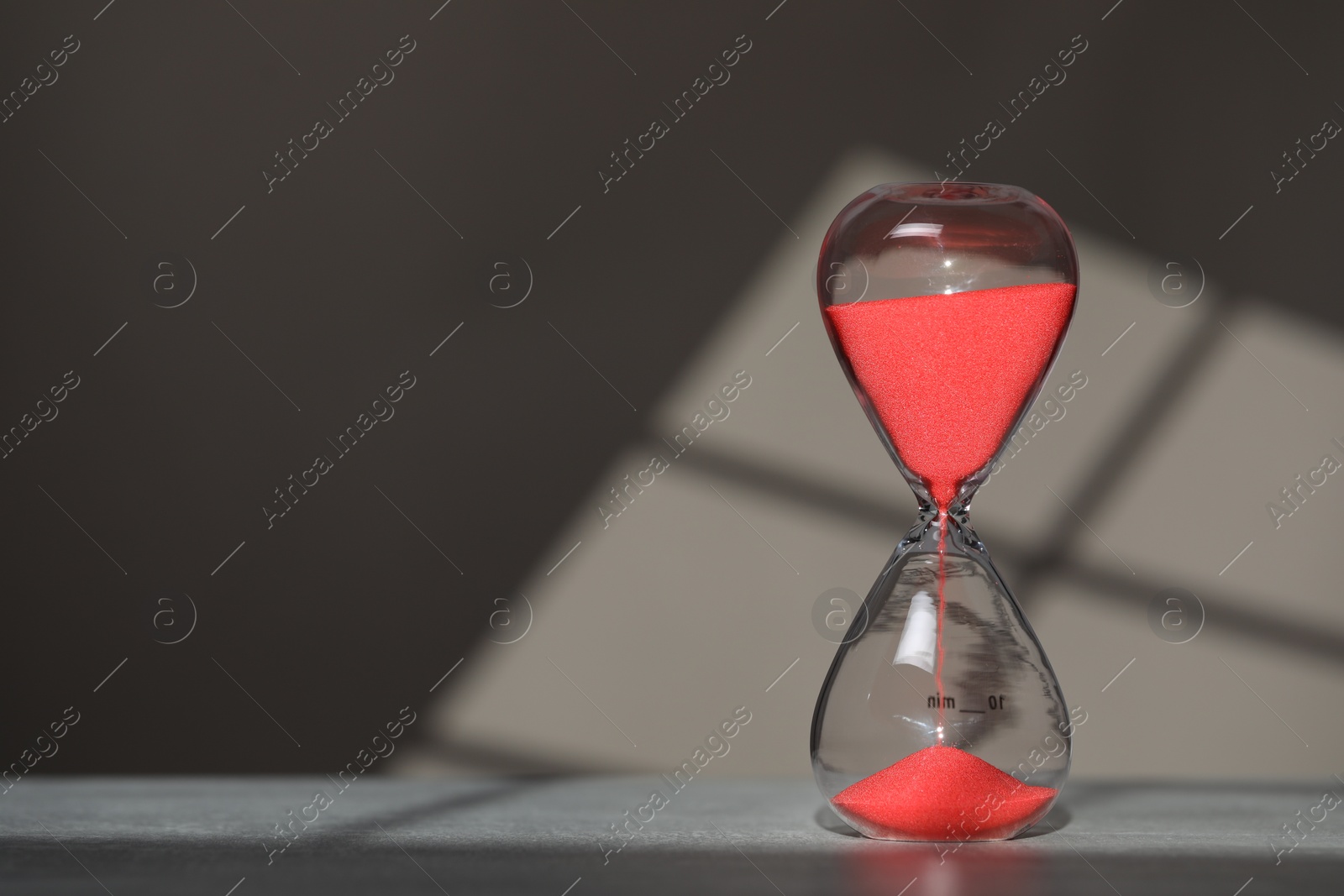 Photo of Hourglass with red flowing sand on table against light grey background, space for text