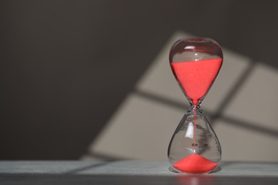 Photo of Hourglass with red flowing sand on table against light grey background, space for text