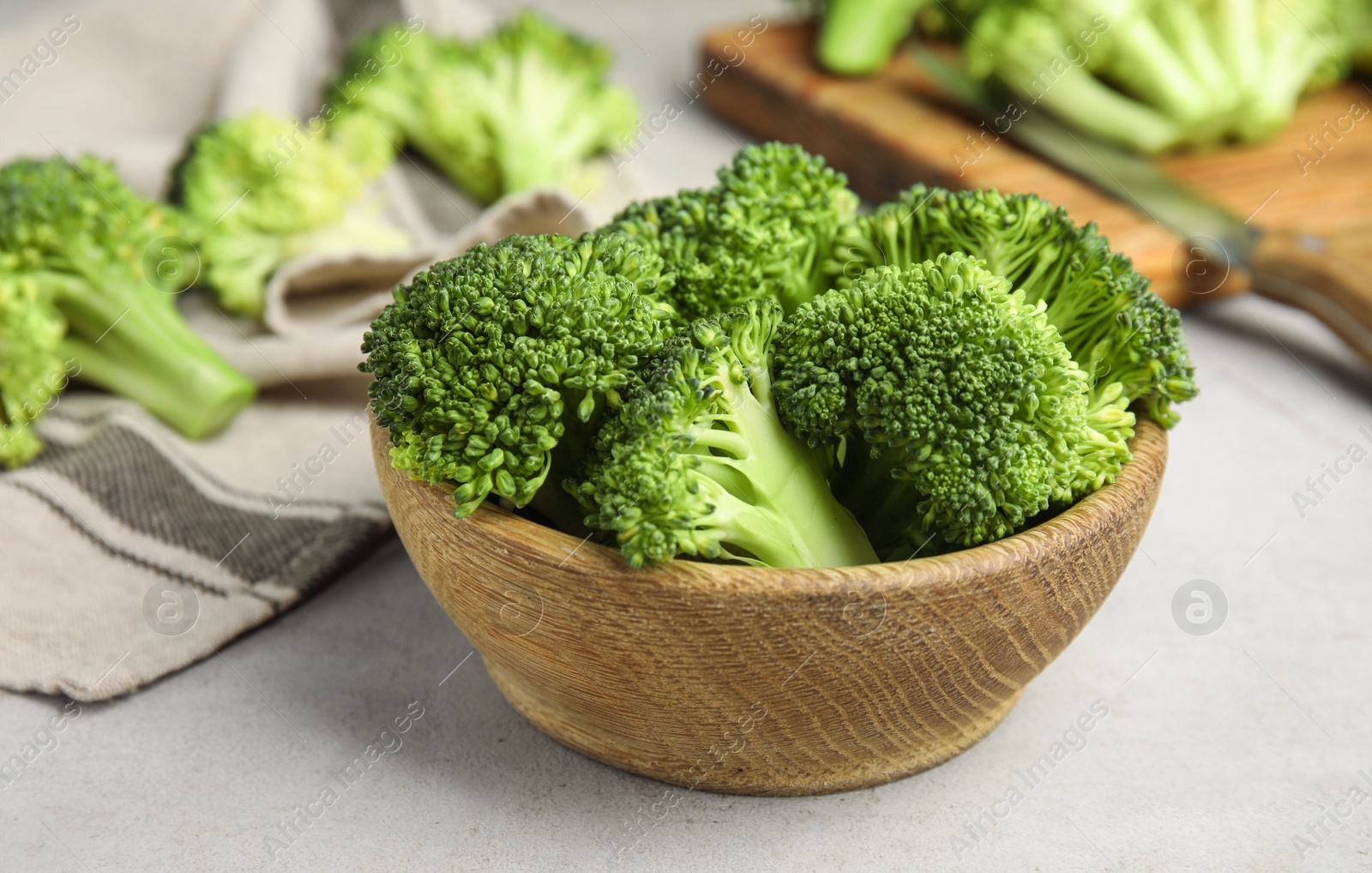 Photo of Fresh green broccoli in wooden bowl on light table