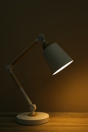 Stylish modern desk lamp on wooden table at night