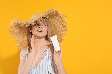 Photo of Beautiful young woman in straw hat holding sun protection cream on orange background, space for text