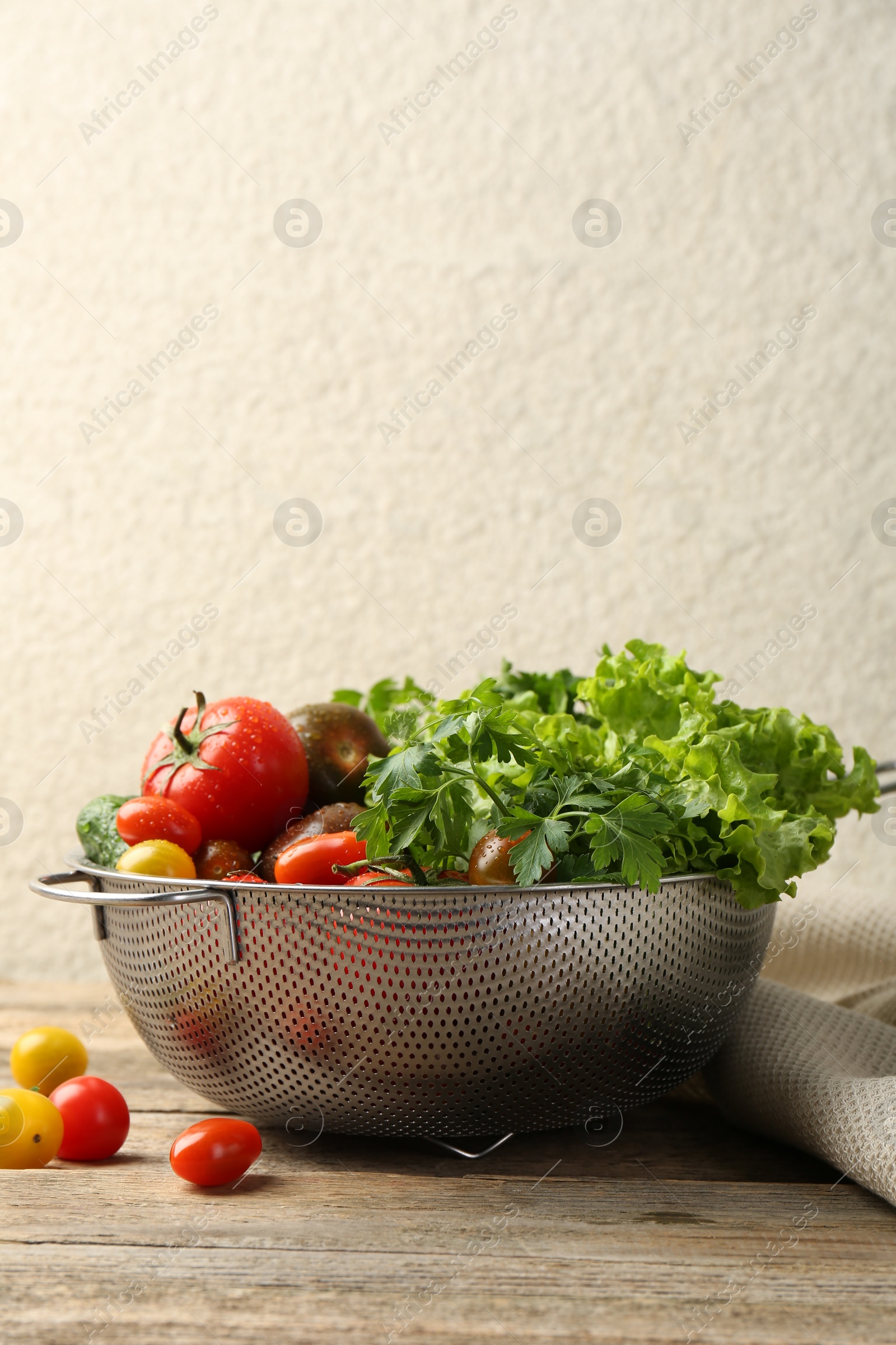 Photo of Wet vegetables in colander on wooden table. Space for text