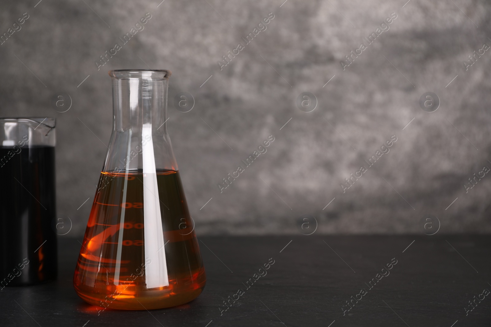 Photo of Beaker and flask with different types of oil on grey textured table