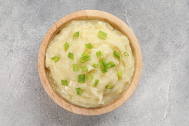 Photo of Bowl of tasty mashed potato with greens on grey marble table, top view