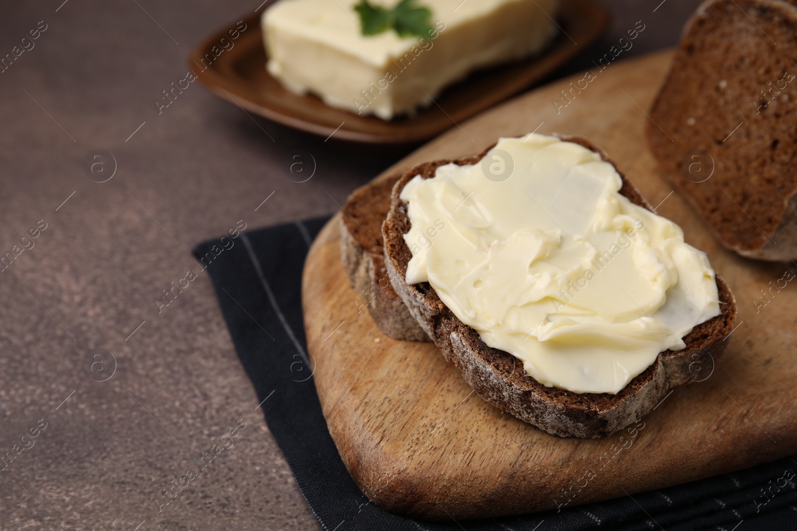 Photo of Slices of tasty bread with butter on grey textured table, closeup. Space for text