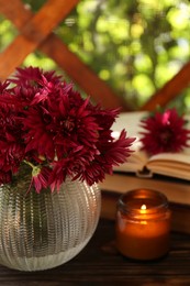 Photo of Beautiful pink chrysanthemum flowers and burning candle on wooden table