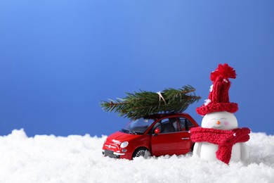 Photo of Cute decorative snowman and toy car with fir tree branches on artificial snow against light blue background, space for text