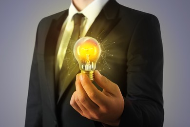 Image of Glow up your ideas. Businessman holding light bulb on grey background, closeup