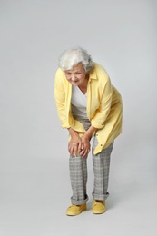 Full length portrait of senior woman having knee problems on grey background