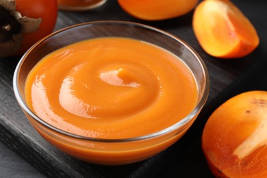 Delicious persimmon jam in glass bowl and fresh fruits on table, closeup