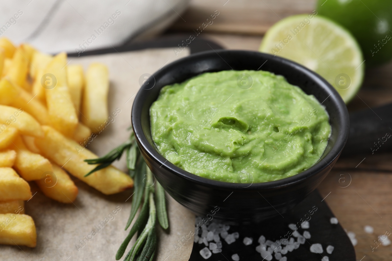 Photo of Serving board with french fries, avocado dip, rosemary and lime served on wooden table, closeup