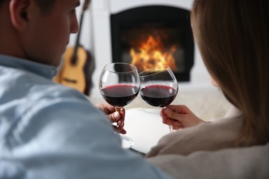Photo of Couple toasting with glasses of wine near fireplace at home, back view