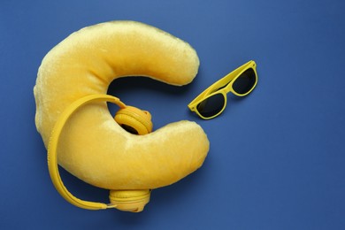 Photo of Yellow travel pillow, headphones and sunglasses on blue background, flat lay