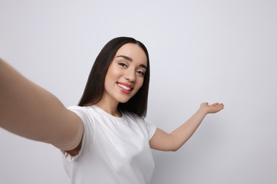 Photo of Smiling young woman taking selfie on white background, space for text