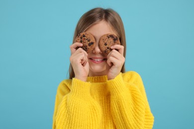 Photo of Girl covering eyes with chocolate chip cookies on light blue background