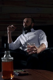 Photo of Man with glass of whiskey and cigar sitting in armchair