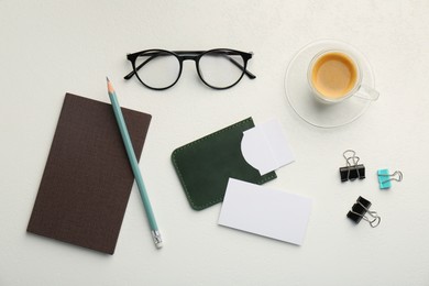 Leather business card holder with blank cards, glasses, coffee and stationery on white table, flat lay