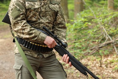 Man with hunting rifle and cartridges wearing camouflage in forest, closeup