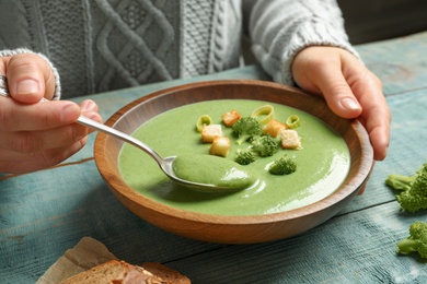 Photo of Woman eating fresh vegetable detox soup made of broccoli with croutons at table, closeup