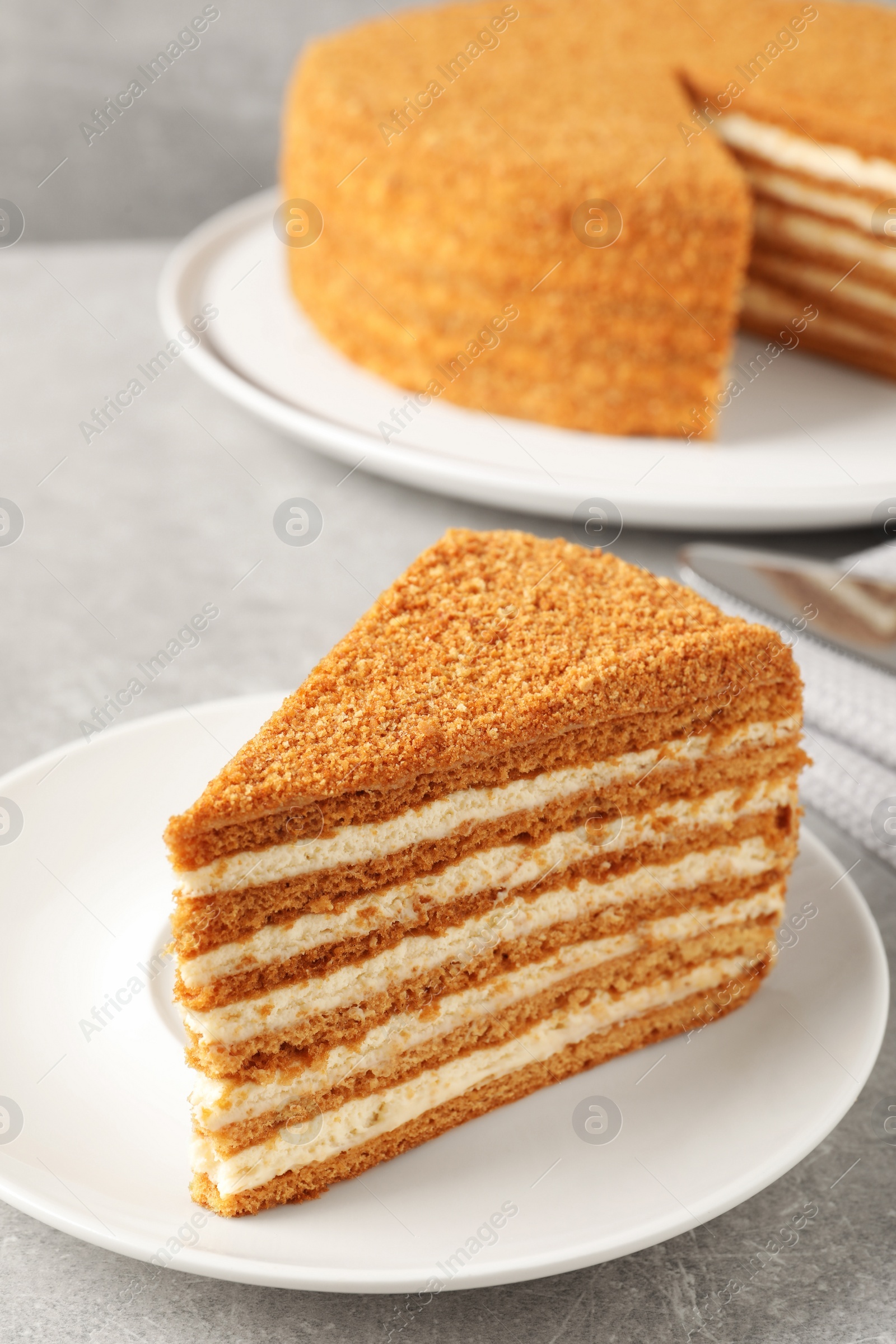 Photo of Slice of delicious layered honey cake served on grey table, closeup