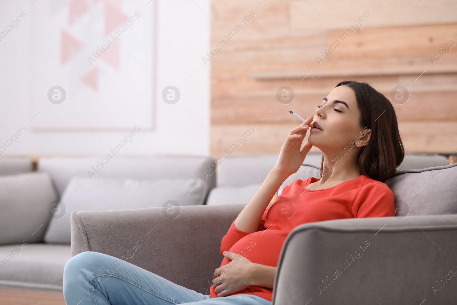 Photo of Young pregnant woman smoking cigarette at home. Space for text