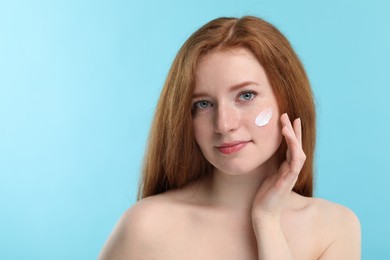 Photo of Beautiful woman with freckles and cream on her face against light blue background. Space for text