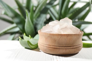 Aloe vera gel in bowl and slices of plant on white wooden table, closeup. Space for text