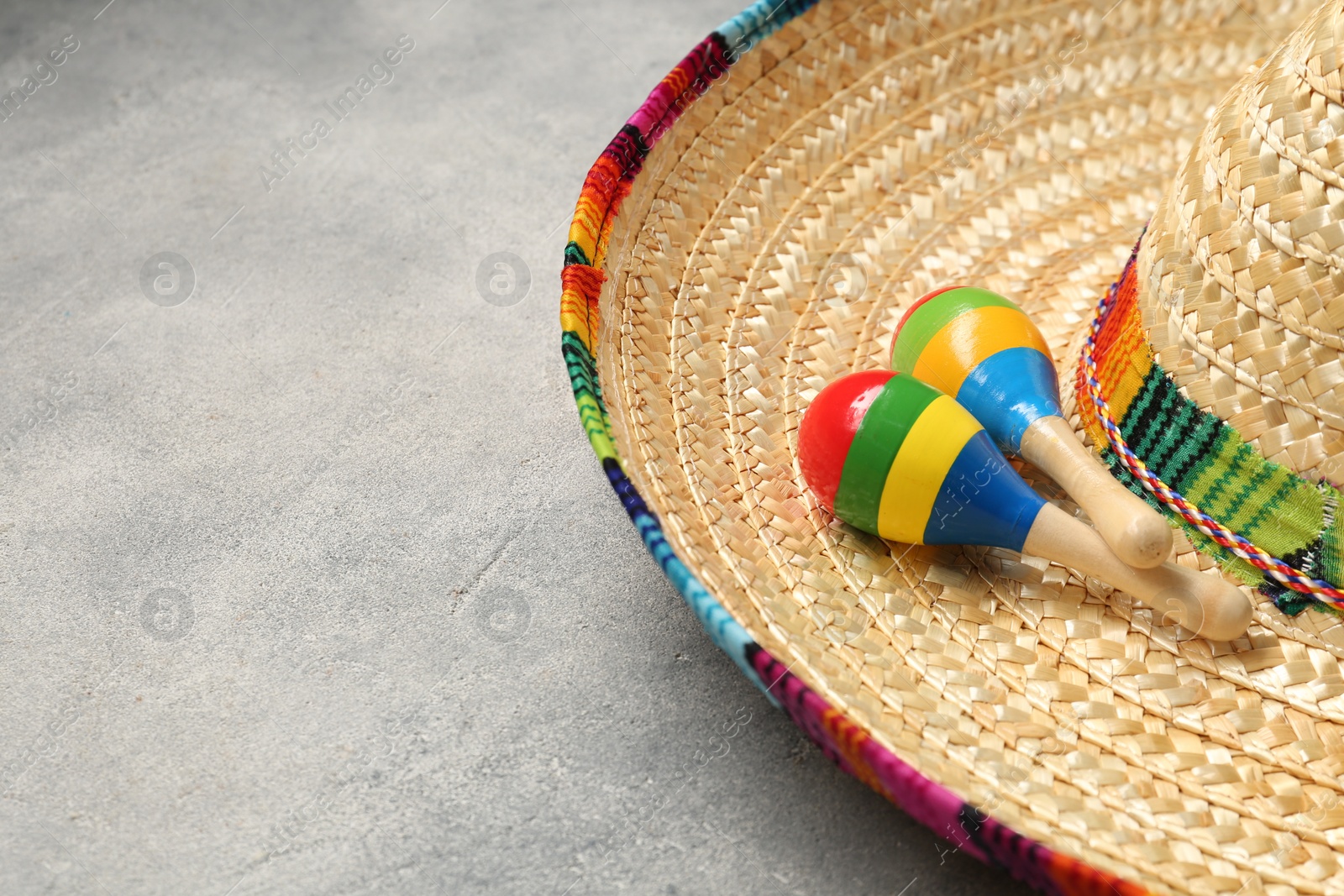 Photo of Mexican sombrero hat and maracas on grey textured table, space for text